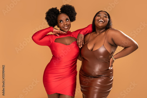 Sexy Plus Size african two women posing in party dresses, having fun together, dancing and smiling. Fashionable girls. Body positive and conscious.