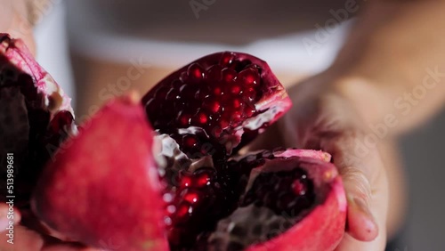 Women's hands have opened a pomegranate and show delicious red grains.White background,close-up, slow motion