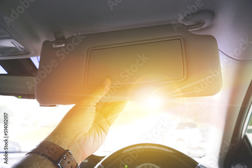 Driver manually adjusting the sun visor in order to block sunlight in a car photo