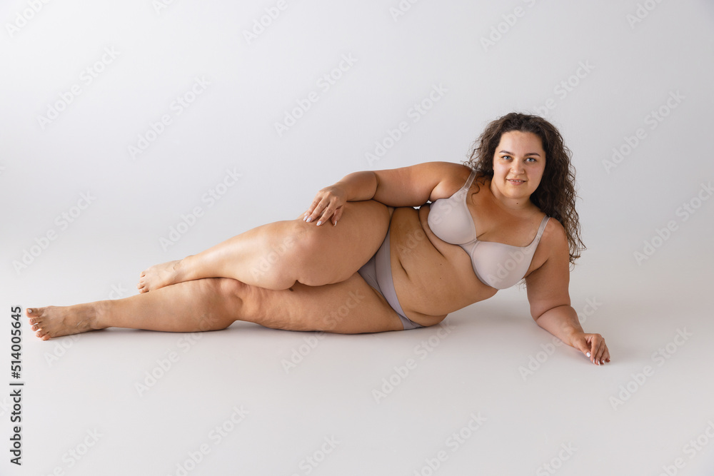 Obraz premium Portrait of beautiful woman with plum figure posing in underwear isolated over grey studio background. Self-acceptance, self-love