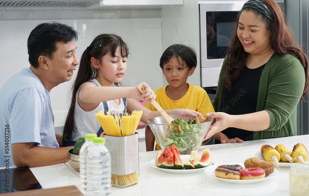 family with healthy cooking concept Father, mother and brother help each other make salad, and their eight-year-old daughter makes a salad for breakfast in the kitchen. family with healthy cooking concept Father, mother and brother help each other make salad, and their eight-year-old daughter makes a salad for breakfast in the kitchen.