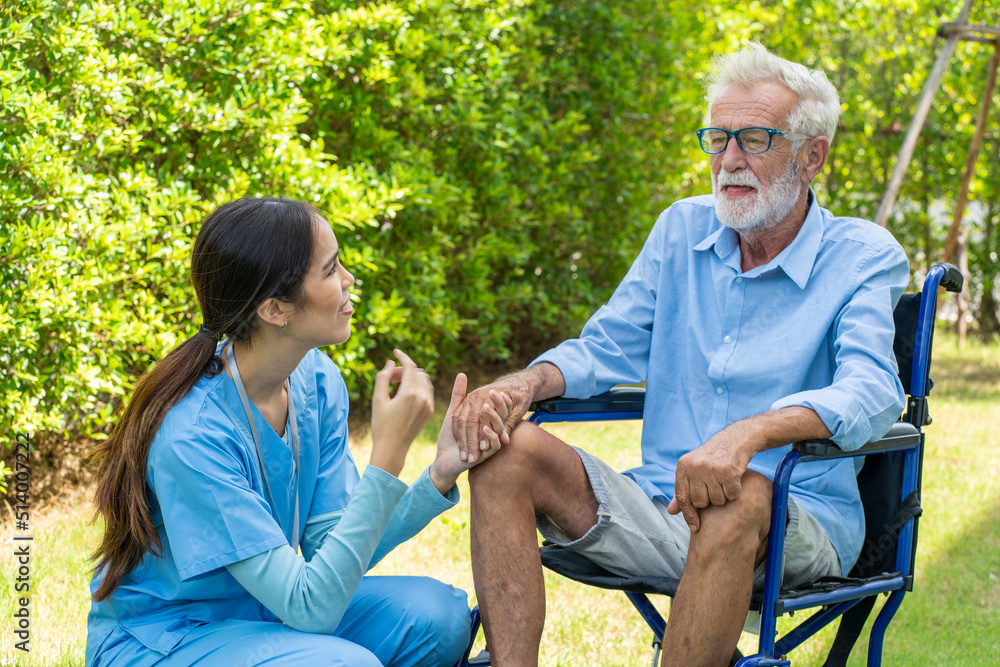 Fototapeta premium Asian nurse takes care An elderly man sitting in a wheelchair holding hands to encourage him to take him out to relax in the garden at Nursing Home