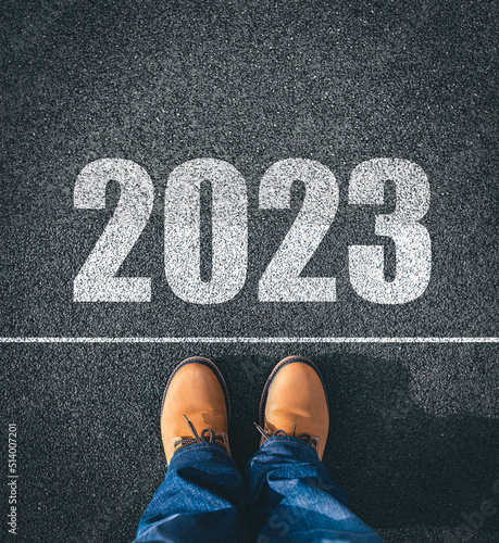 Obraz na płótnie New year 2023, concept. 2023 inscription on the asphalt. The man in boots takes a step into the new year 2023. w salonie