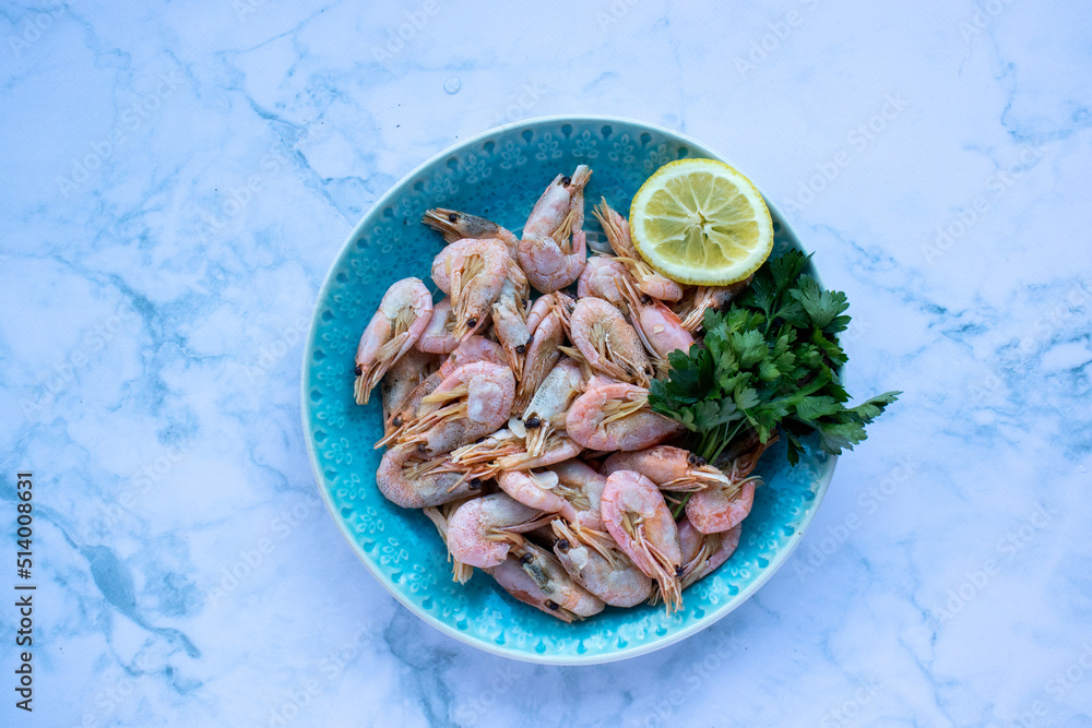Сooked shrimp with parsley and lemon in a blue ceramic bowl on a white marble table background. Healthy Mediterranean seafood. Top view, flat lay, copy space Сooked shrimp with parsley and lemon in a blue ceramic bowl on a white marble table background. Healthy Mediterranean seafood. Top view, flat lay, copy space