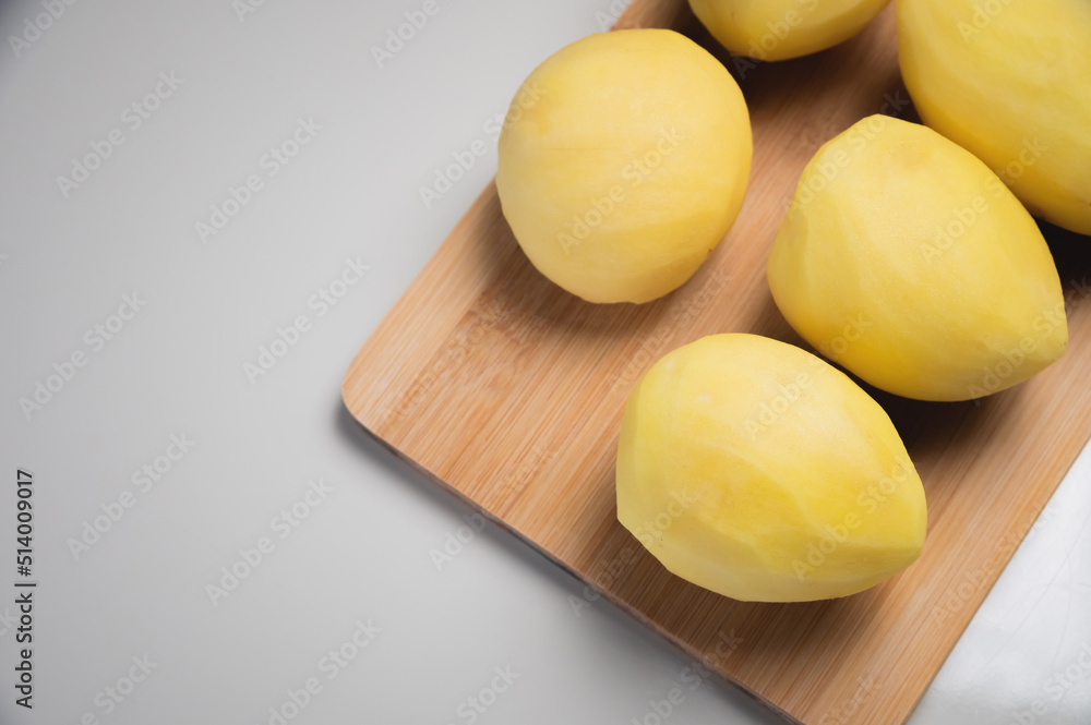 Peeled fresh potatoes lie on a wooden cutting board on a white table