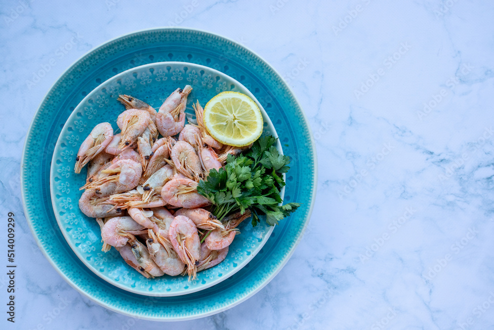 Сooked shrimp with parsley and lemon in a blue ceramic bowl on a white marble table background. Healthy Mediterranean seafood. Top view, flat lay, copy space Сooked shrimp with parsley and lemon in a blue ceramic bowl on a white marble table background. Healthy Mediterranean seafood. Top view, flat lay, copy space
