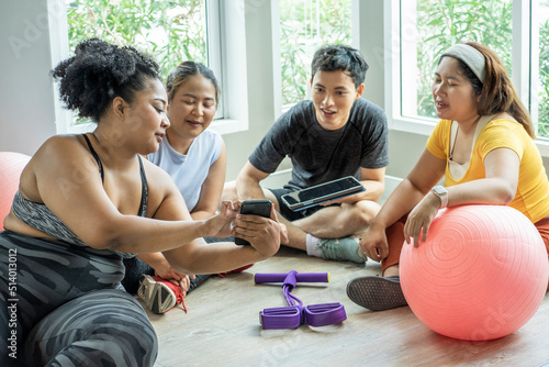 Three fat women, plus size women wearing sportware outfits talking with trainer hold tablet talking togetther in class. Healthy weight loss in the gym Relationship concept and fat girl exercising photo