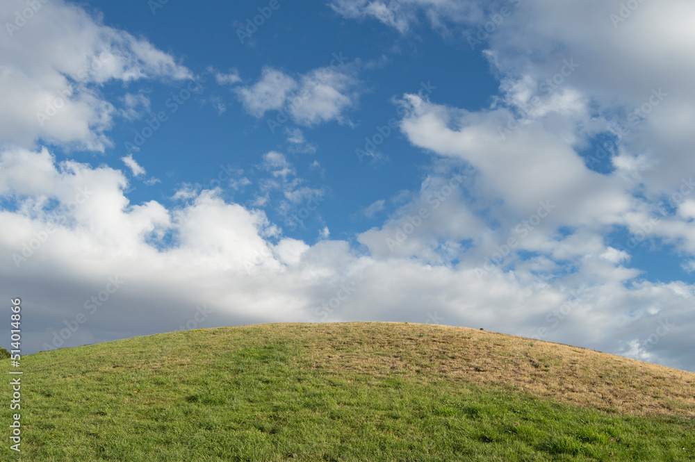 mound with grass meadow over sky with clouds in a park