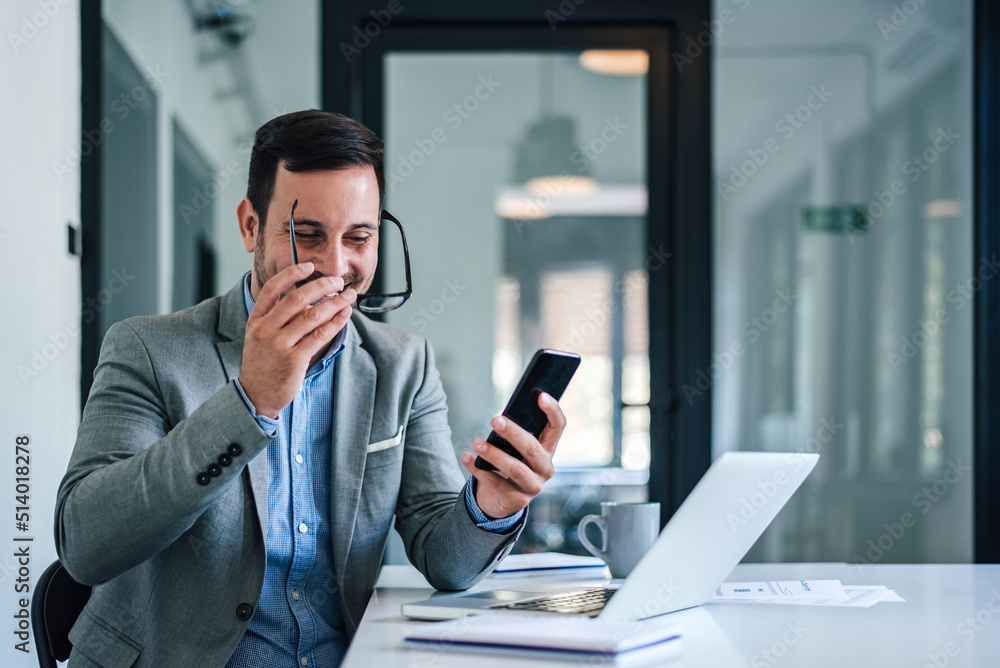 Happy manager wearing eyeglasses while text messaging on cellphone at office Happy manager wearing eyeglasses while text messaging on cellphone at office