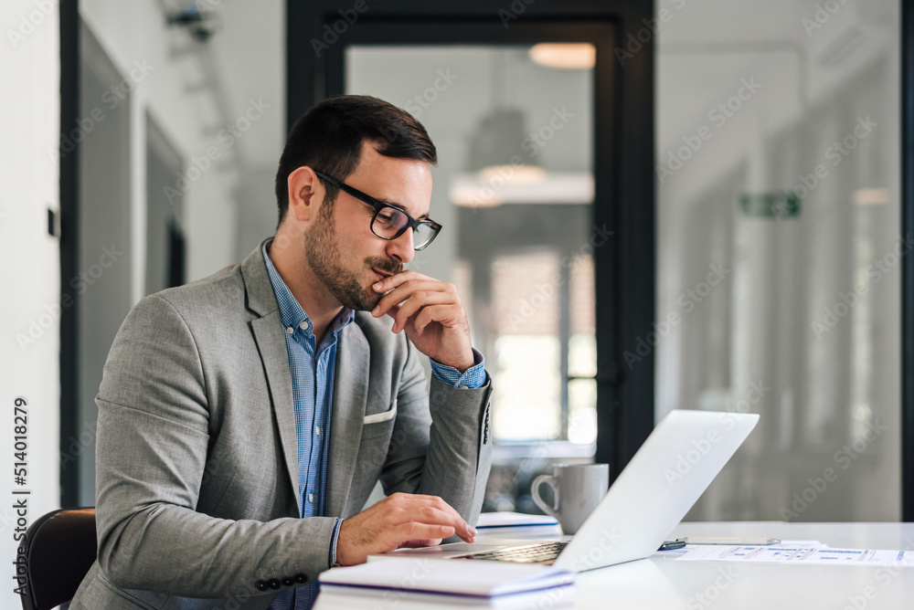 Confident entrepreneur scrolling on laptop while working at desk in office Confident entrepreneur scrolling on laptop while working at desk in office