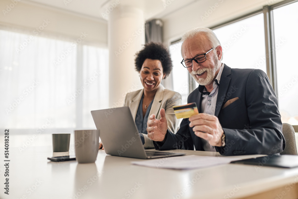 Male and female colleagues paying online through credit card on laptop at office Male and female colleagues paying online through credit card on laptop at office