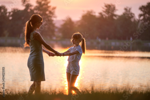 Happy mom and daughter girl relaxing holding hands enjoying time together in summer park at sunset. Family love and relationship concept