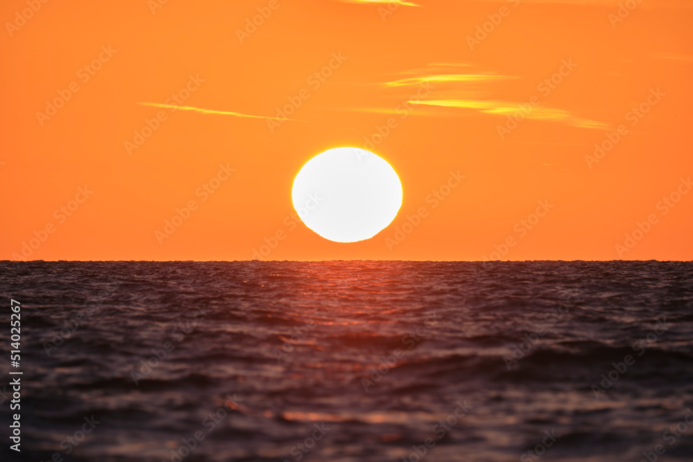 Ocean sunset. Big white sun on dramatic bright sky background, soft evening cloud over sea dark water
