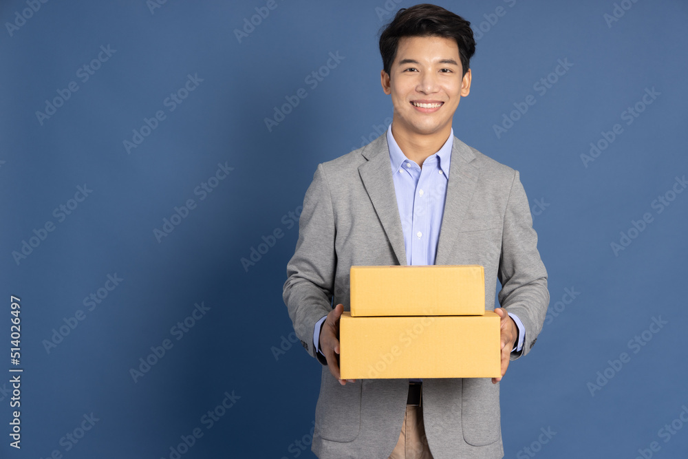 Asian businessman holding package parcel box isolated on blue background, Delivery courier and shipping service concept Asian businessman holding package parcel box isolated on blue background, Delivery courier and shipping service concept