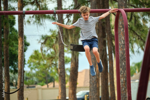 Fotografia Young handsome smiling teenage boy jumping out of the swings on summer vacations sunny day