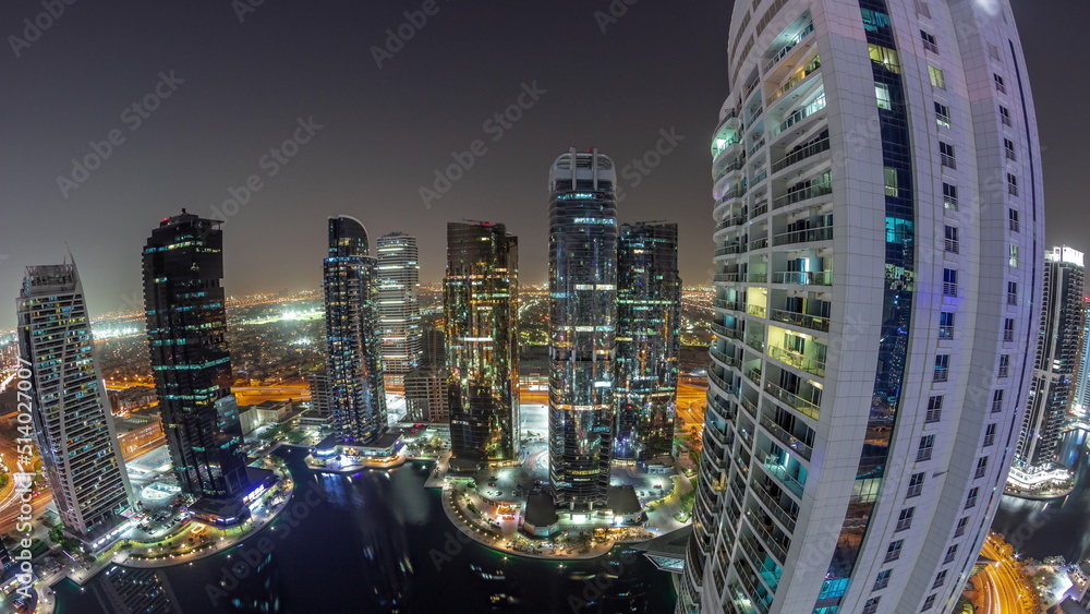 Fototapeta premium Panorama of tall residential buildings at JLT aerial night timelapse, part of the Dubai multi commodities centre mixed-use district.