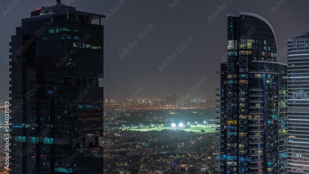 Aerial view of housing development promenade with JLT district skyscrapers and artificial lake with a park night timelapse.