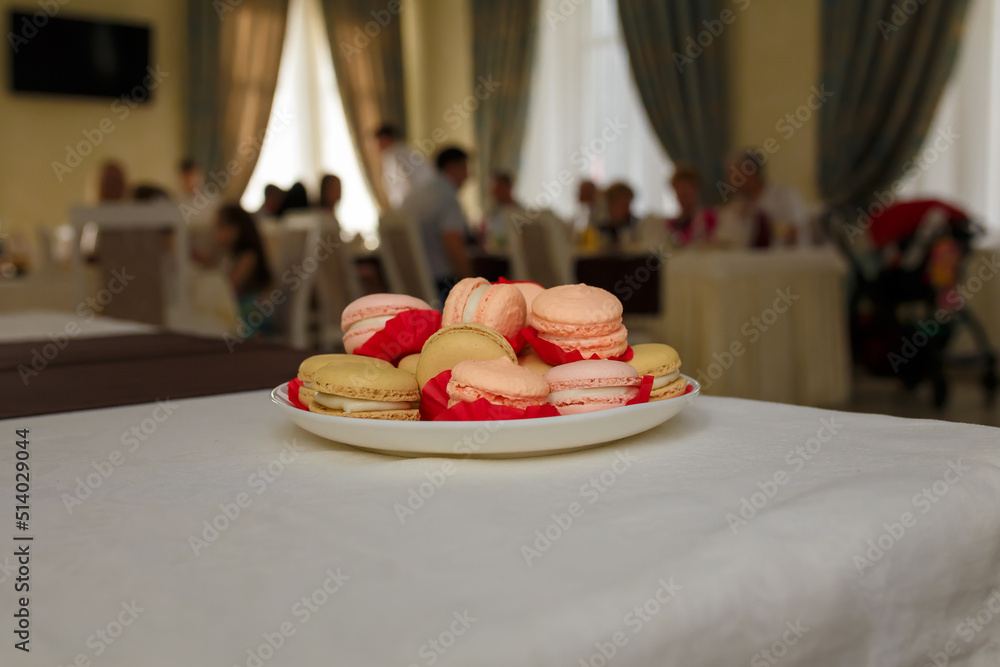 Birthday treat. White plate with french macarons or macaroons. Dessert for birthday party. Unrecognizable people, guests having dinner on background Birthday treat. White plate with french macarons or macaroons. Dessert for birthday party. Unrecognizable people, guests having dinner on background