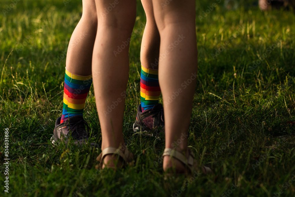LGBT lesbian couple with colorful rainbow socks standing together in park grass, only legs visible.