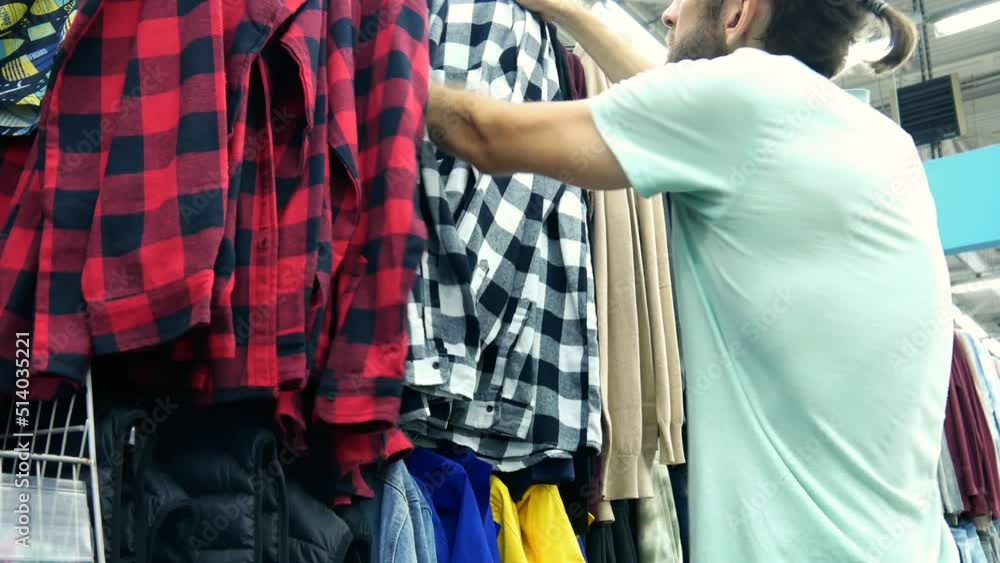 A bearded man choosing a checkered shirt in a clothing store A bearded man choosing a checkered shirt in a clothing store