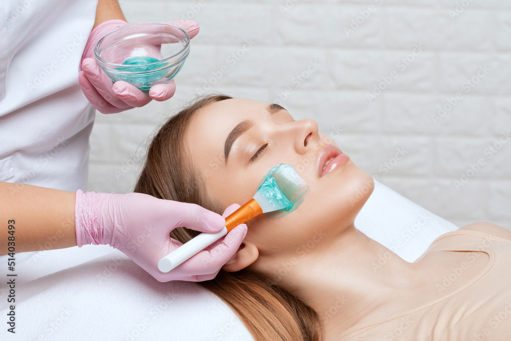 Beautician makes a face mask of a woman to rejuvenate the skin. Cosmetology treatment of skin on the face and body. Beautician makes a face mask of a woman to rejuvenate the skin. Cosmetology treatment of skin on the face and body.
