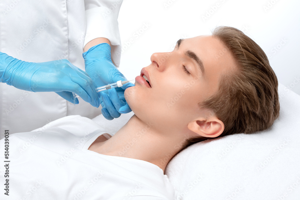 The cosmetologist makes injections for lip augmentation and anti-wrinkle in the nasolabial folds of a man. Male cosmetology in a beauty salon. The cosmetologist makes injections for lip augmentation and anti-wrinkle in the nasolabial folds of a man. Male cosmetology in a beauty salon.
