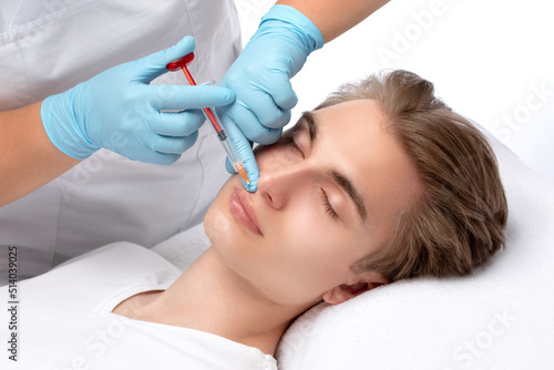 The cosmetologist makes injections for lip augmentation and anti-wrinkle in the nasolabial folds of a man. Male cosmetology in a beauty salon.