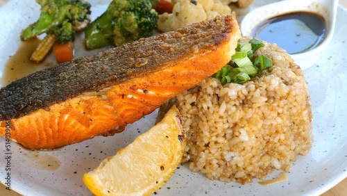 Grilled salmon fillet with fried garlic rice, spices and vegetables. Healthy seafood rich omega-3. Grilled salmon fish steak with lemon and sauce on plate in restaurant.