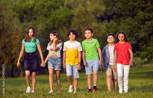 Several teenagers boys and girls from elementary school walking with friends smiling stepping forward have fun taking break between lessons or summer vacation in park. Children portrait