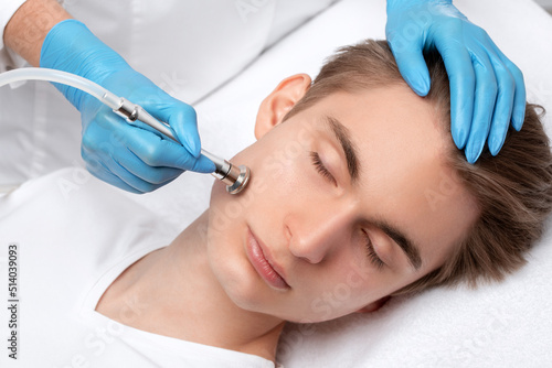 A cosmetologist is making the procedure Microdermabrasion of the facial skin in a beauty salon. Cosmetology for men and professional skin care.