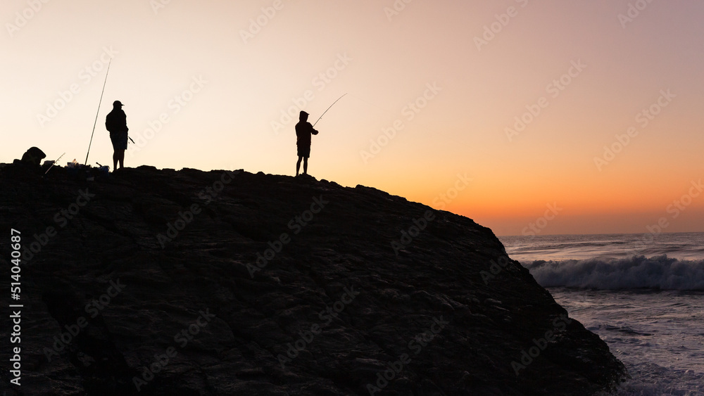 Beach Ocean Dawn Morning Two Fishermen Figures Silhouetted Fishing Off  Rocky Coastline a Scenic Sky Color Landscape.