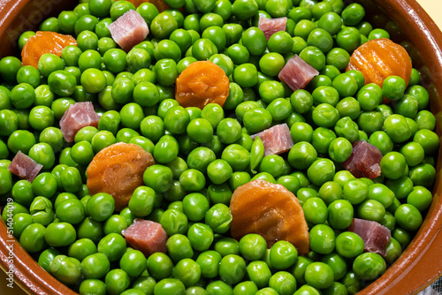 Green peas with serrano ham and carrot on table