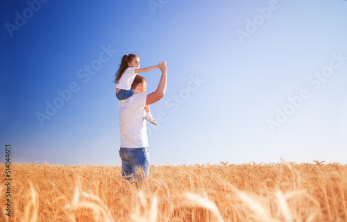 Happy father and daughter walk in the summer field. Nature beauty, blue sky and field with golden wheat. Outdoor lifestyle. Freedom concept. © Dmytro Sunagatov
