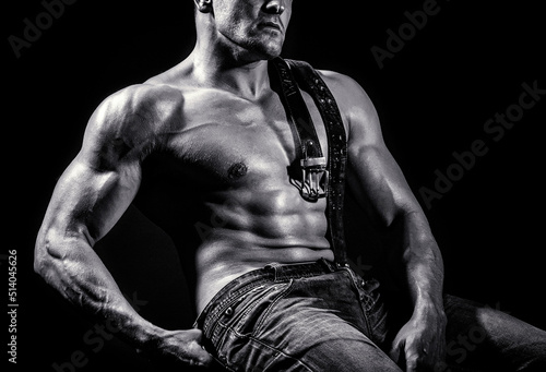 Strong athletic man showing muscular body, sixpack abs. Torso with six packs looks attractive on black background. Leather belt, jeans. Torso six packs attractive. Sport workout bodybuilding concep