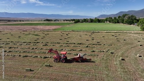 Aerial farm tractor bale alfalfa hay tractor. Aerial rural farming community agricultural economy. Early Spring summer season weather mountain valley agriculture field. Seasonal rural farm city.