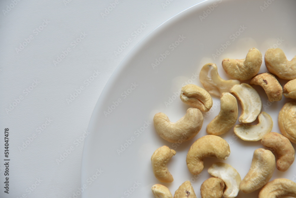 Cashew nuts on a white plate in a group of loose Cashew nuts on a white plate in a group of loose