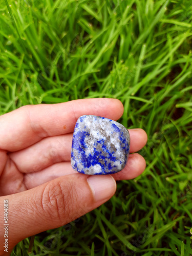 Lazurite mineral stone in the hand on green grass background, natural gemstone for healing, meditation, altar, spiritual practice, reiki, ritual.