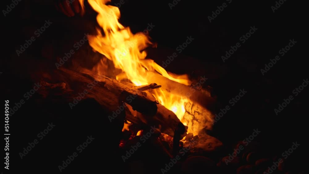 A man tosses wood into the fire. Sparks from the embers fly beautifully into the darkness. Time lapse photography. A night campfire by the sea A man tosses wood into the fire. Sparks from the embers fly beautifully into the darkness. Time lapse photography. A night campfire by the sea
