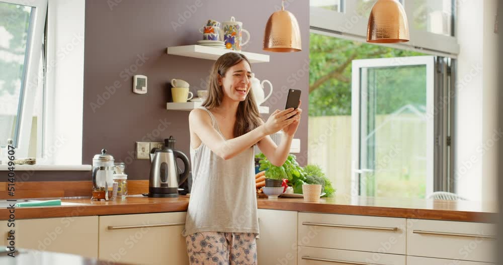 A happy young woman smiling and waving during a video call on her smartphone A happy young woman smiling and waving during a video call on her smartphone