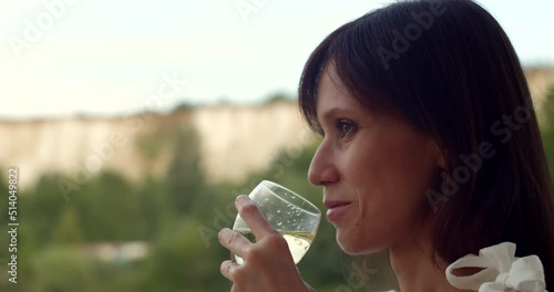 Woman relaxing with cup of wine on terrace looking on lake, godless hedonism concept
