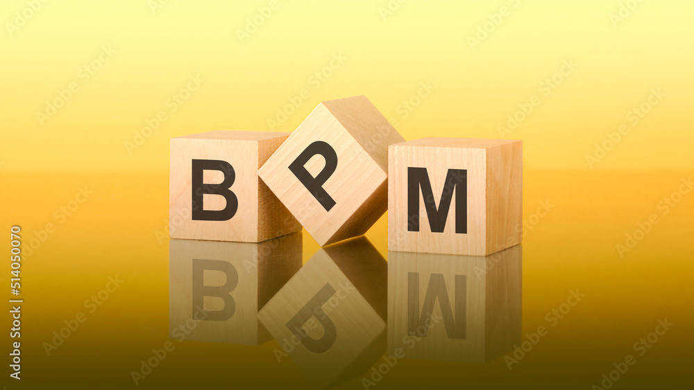 Three wooden cubes with the letters BPM on the bright yellow surface. the inscription on the cubes is reflected from the yellow surface of the table Three wooden cubes with the letters BPM on the bright yellow surface. the inscription on the cubes is reflected from the yellow surface of the table