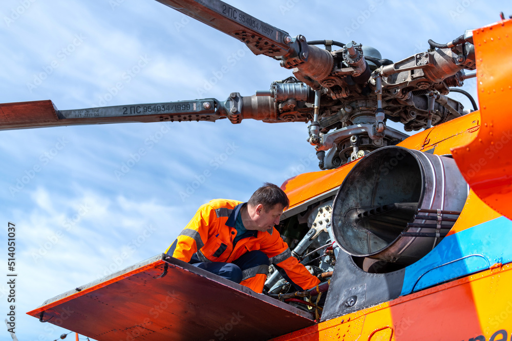 Technician - ground personnel at the airport checks the engine of the helicopter. Taken in backlit and sun glare.  Helicopter maintenance.