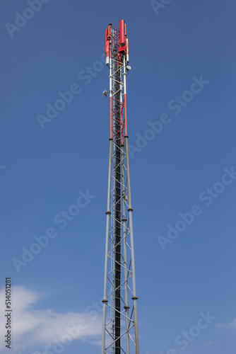 Antennenmast für Mobiltelefone als Gitterrohrmast rot und weiß gestrichen vor einem blauen Himmel.