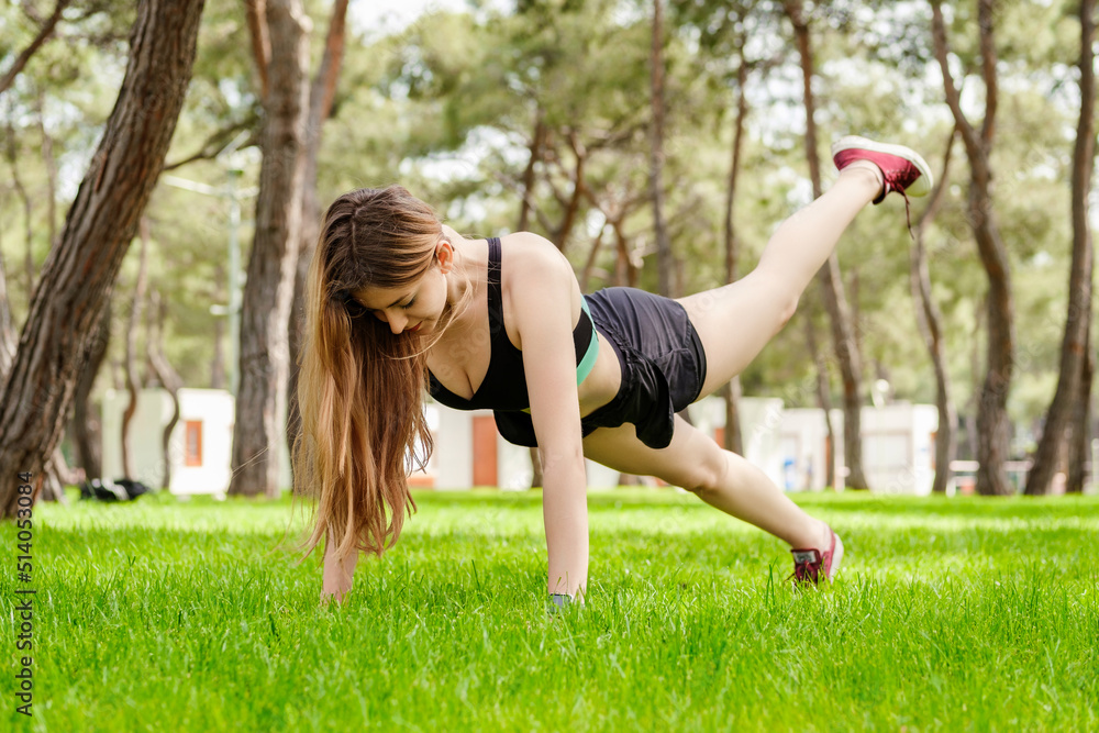 Obraz premium Young beautiful woman wearing sportive clothes on city park, outdoors woman doing push ups with one leg up. Outdoor sports, healthy life concepts.
