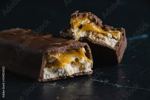 Delicious chocolate bar with caramel and peanuts close up on dark concrete background with copy space