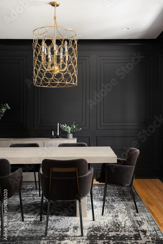 Fototapeta A cozy dining room with a gold chandelier above a wooden table and black wainscoting walls