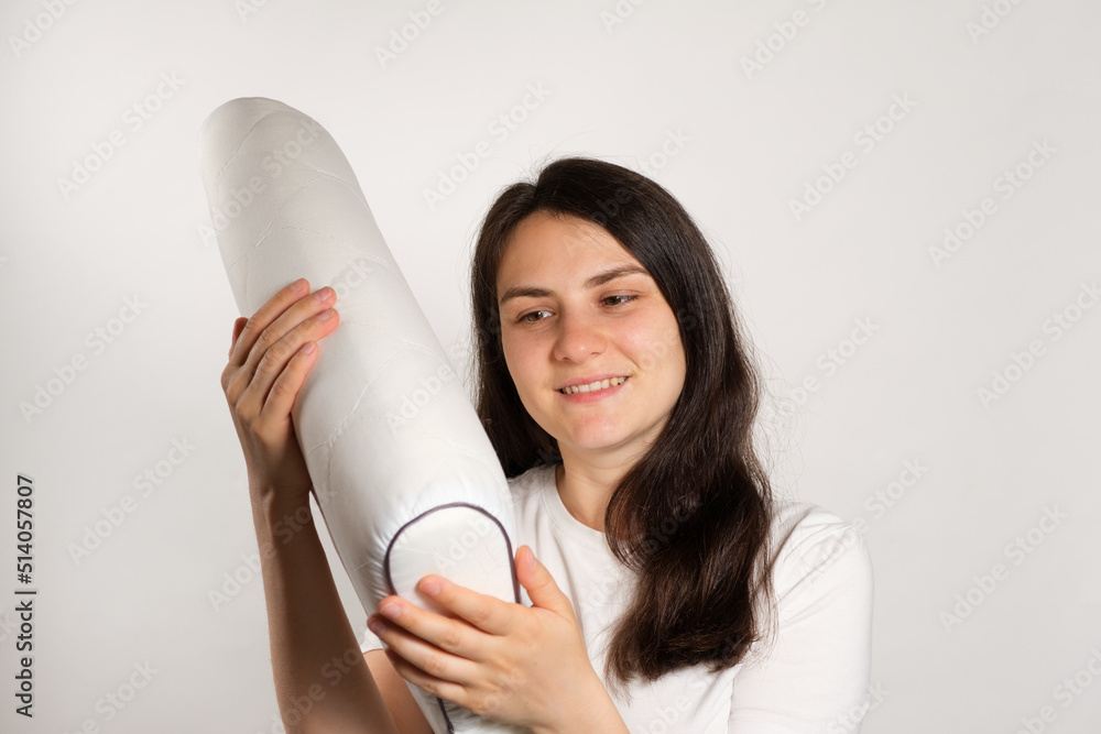 Fototapeta premium A woman holds an orthopedic pillow made of memory foam and smiles. Choosing the right pillow for healthy sleep.