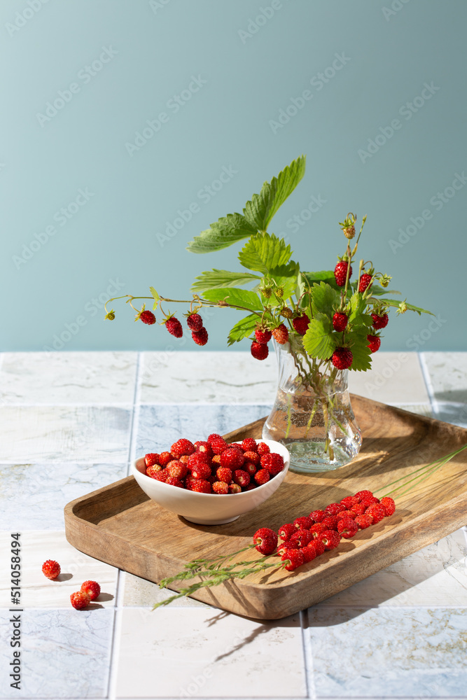 Φωτογραφία Bouquet of wild strawberry berries with leaves  in glass vase and lot of berries on wooden tray