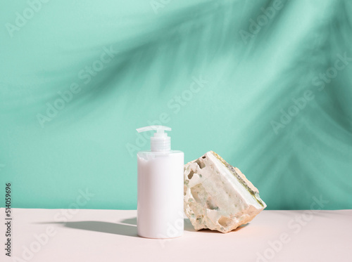 Cosmetic bottle of white color on a podium made of natural stone, blue background with deep shadows