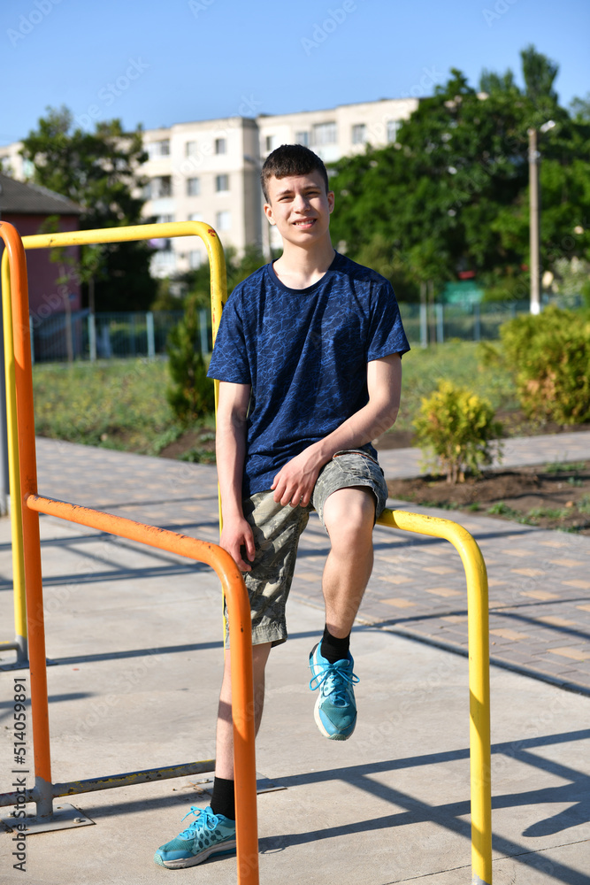 Fototapeta premium a teenage boy trains on a sports ground outdoors, he does physical exercises, a healthy lifestyle, a bright sunny day in summer